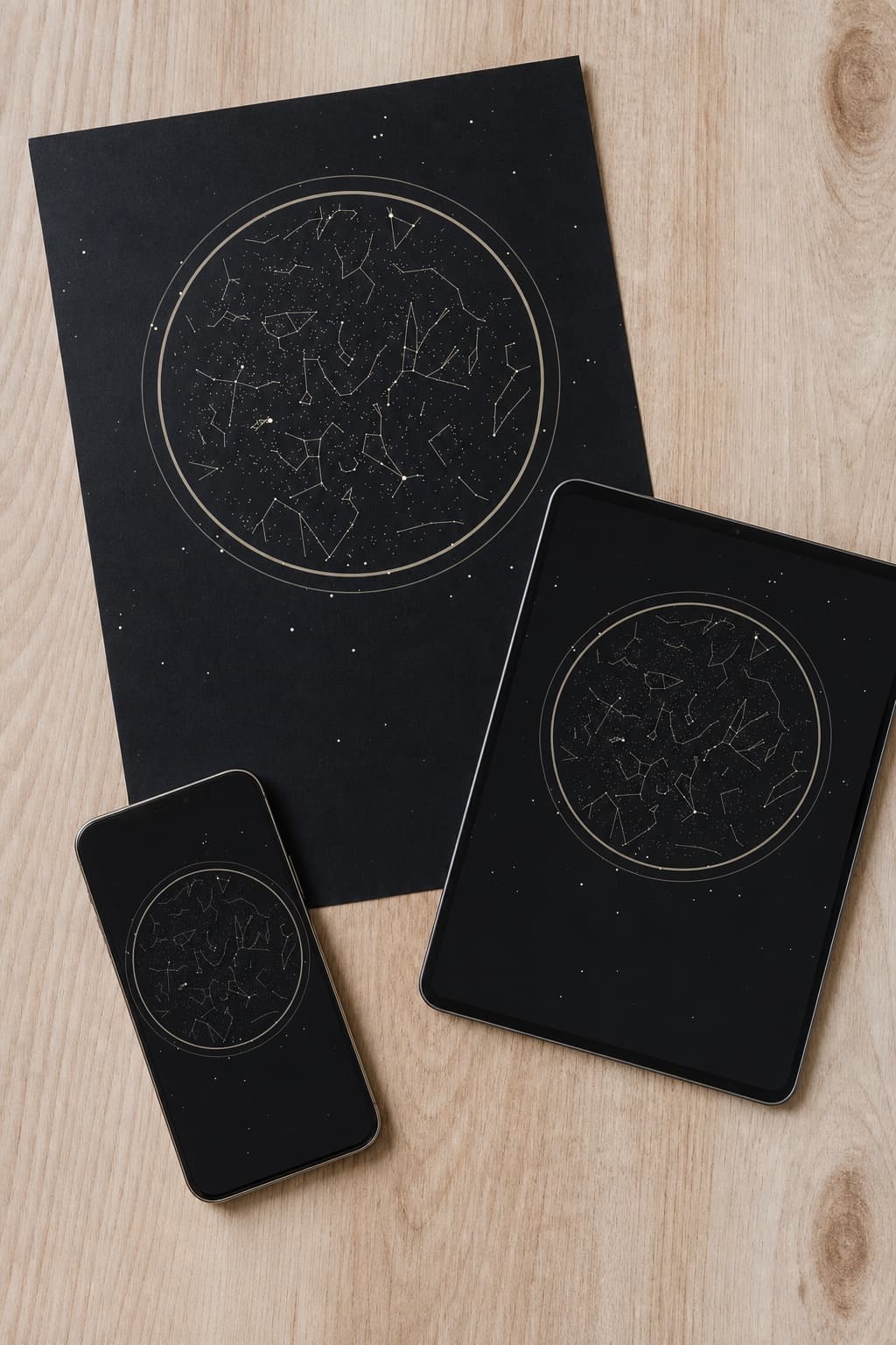 A printed star map on a wooden desk beside a tablet and a phone showing the same sky.