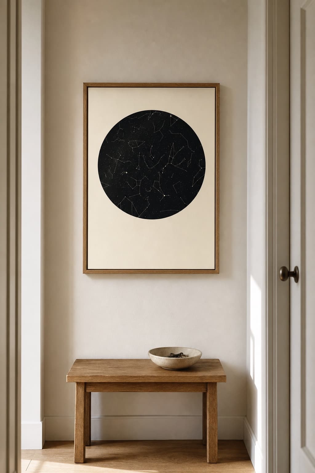 A warm white star map with a black sky disc, framed in oak, hanging above a bench in a hallway.