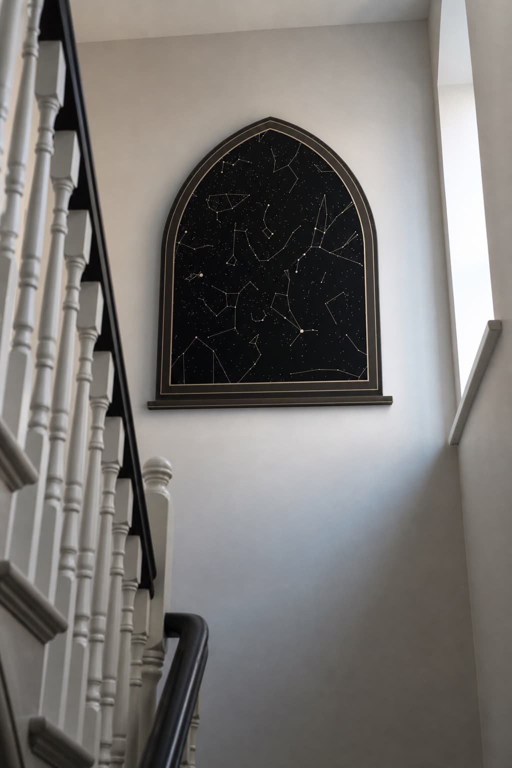 An arch-shaped black star map hanging on a tall, plain stairwell wall.